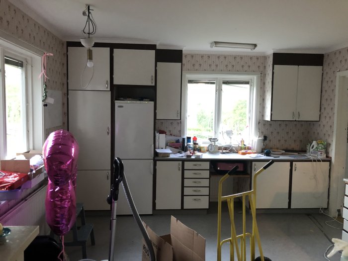 Kök i förberedelse för renovering med rörigt utseende, tomma väggar och oorganiserade köksutrustning och lådor.