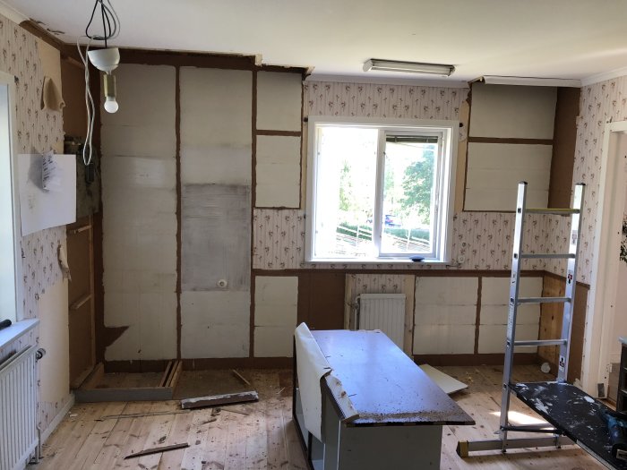 Kök under renovering med tomma väggar och demonterade skåp, stege i mitten.