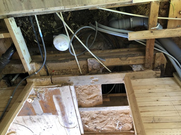 Rivningsarbete i golv med synliga gamla och nya rör för vatten och avlopp samt elledningar.