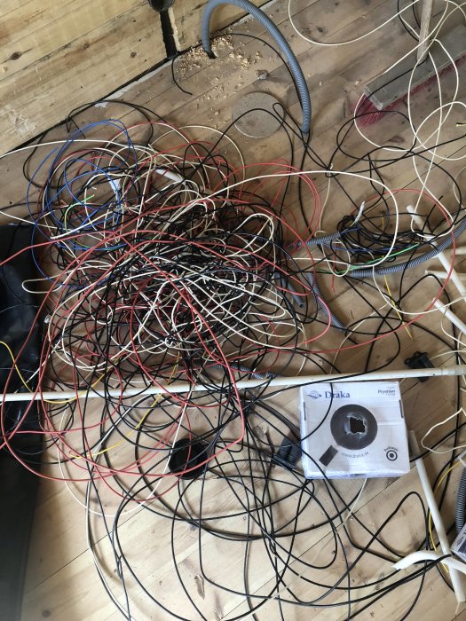 En stor hög med elektriska kablar och ledningar i olika färger på ett trägolv, symbolen för elomläggning.