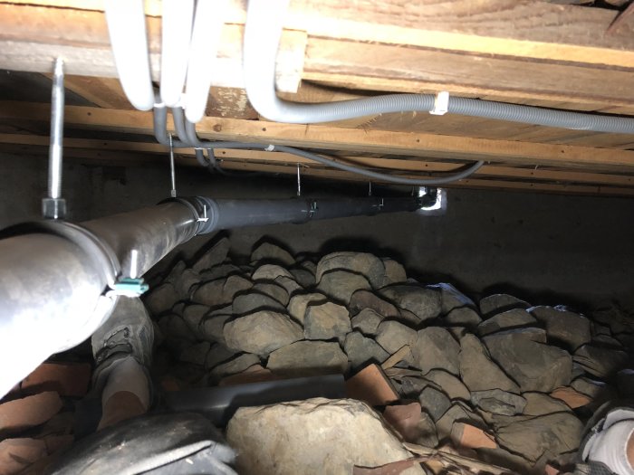 Ny elektrisk kabeldragning i krypgrund med synliga rör och kablar mot stenig grund.