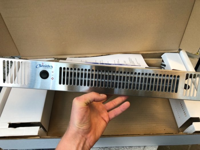 Hand håller en liggande vattenburen radiator med 230v fläkt för badrumsprojekt.