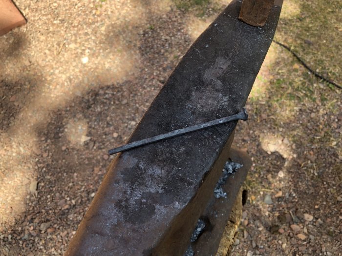 Gammal rakad spik som ligger på en ässja, mot en suddig bakgrund av grus och gräs.