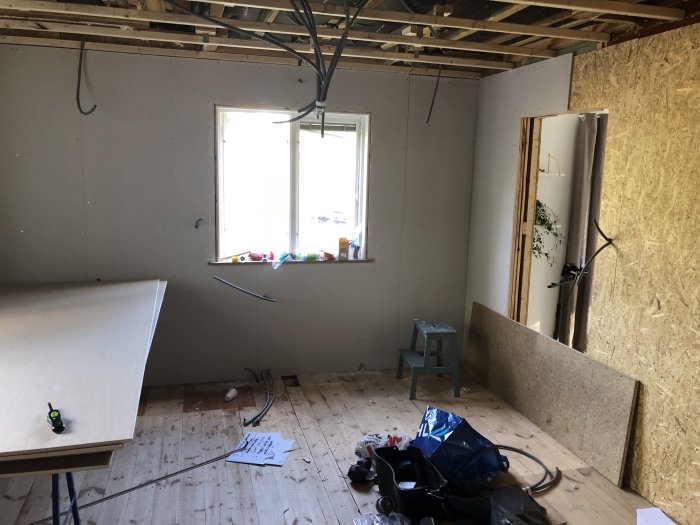 Renoveringsrum med nygipsade väggar, oskivad väggdel, verktyg och byggmaterial på golvet.