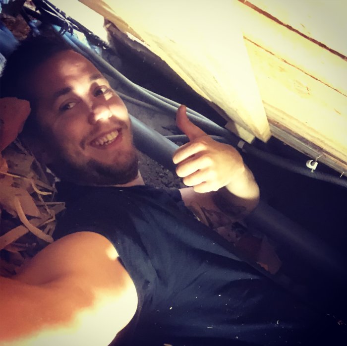 Person ger tummen upp i krypgrund med synlig isolering och träreglar.