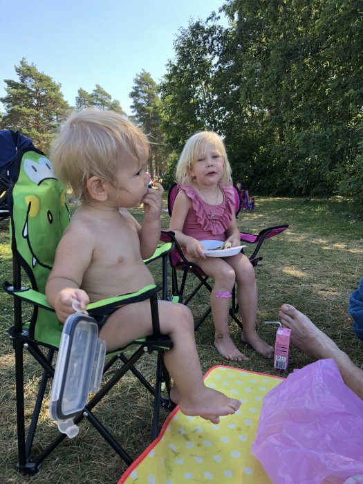 Två barn som sitter och äter i hopfällbara stolar utomhus under en paus i familjens renoveringsprojekt.