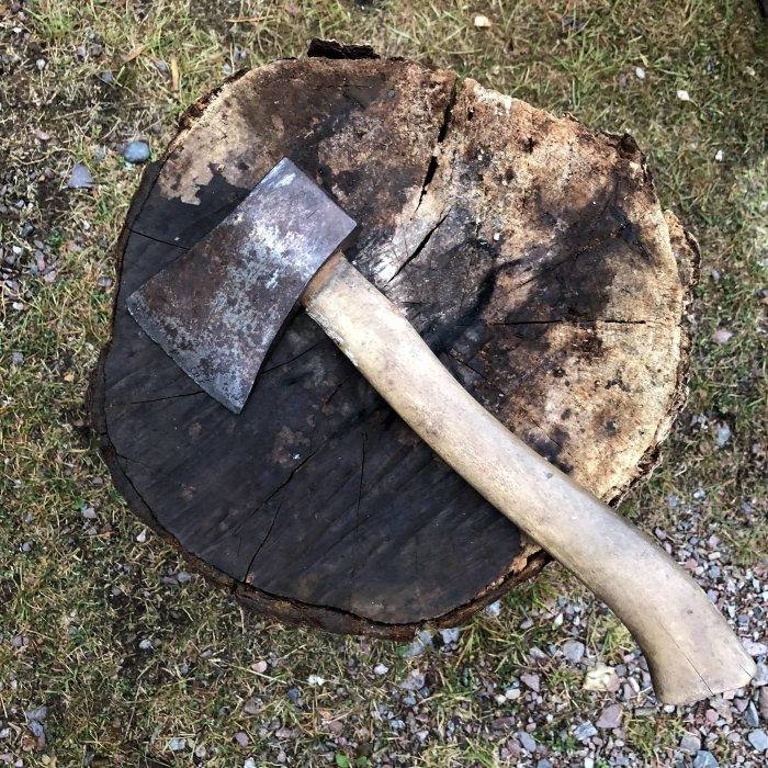 Yxa med träskaft på en avhuggen trädstubbe mot gräsigt underlag.