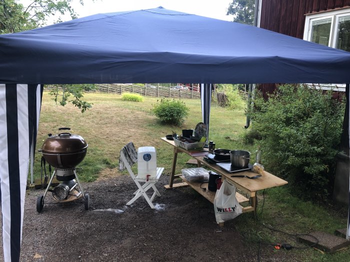 Utekök med tälttak, grill och provisorisk arbetsbänk med matlagningsgrejer i trädgården.