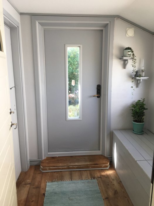 Nymålad farstu med gråa väggar, vit dörr, trägolv och inredningsdetaljer.