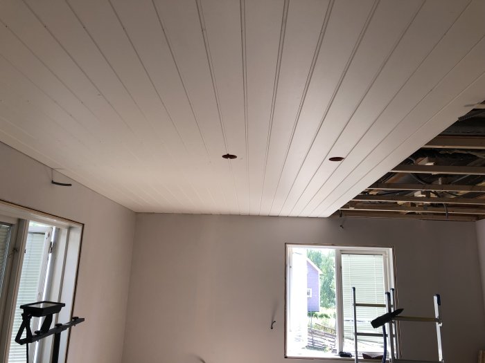 Renoverat rum med nyinstallerat vitt träpaneltak med utmarkerade spottar och en stege i förgrunden.