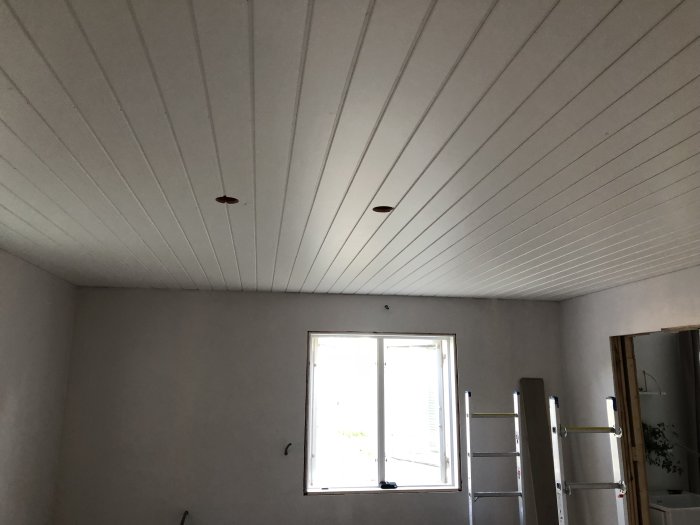 Nytt vitt tak med utmarkerade platser för spotlights i ett rum med fönster och stege.