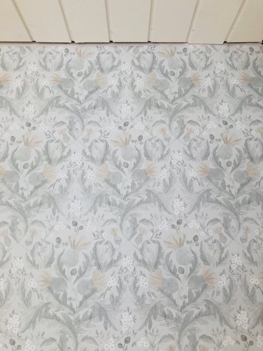 Tapet med blommönster i naturfärger på en vägg, klar för rummets renovering.