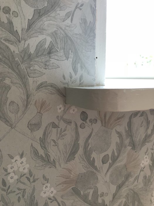 Tapet med blommönster i grå och vita toner nära ett fönster, i naturlig färg.