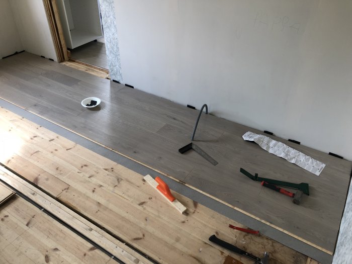Installation av ljusgrå 1-stav parkettgolv med verktyg och byggmaterial synliga.