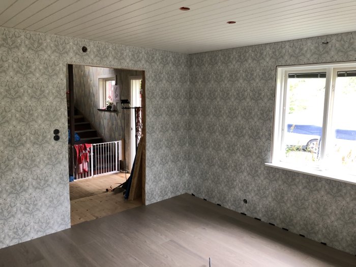 Rum under renovering med nyinstallerad ljusgrå 1-stavs parkettgolv och blommigt tapetserade väggar.