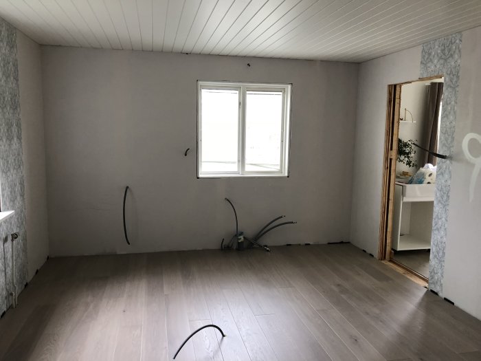 Ljusgrå 1-stavs parkettgolv i tomt rum med vita väggar och kablar på golvet.