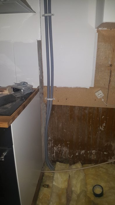 Installation av nya gråa plaströr bredvid befintliga kopparrör längs en vägg med synliga isoleringsmaterial.