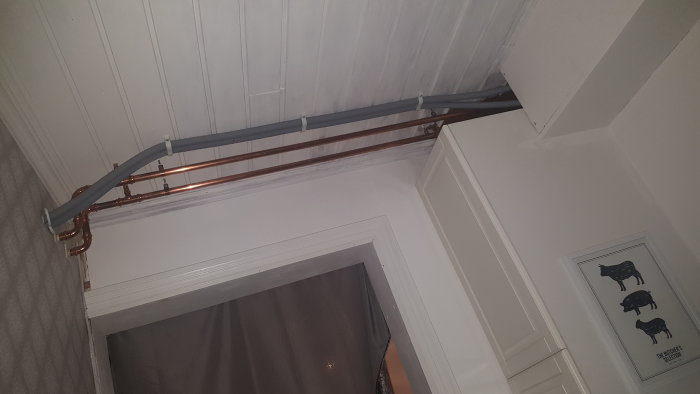VVS-arbete med nya plaströr intill befintliga kopparrör i ett taknära hörn av ett rum.