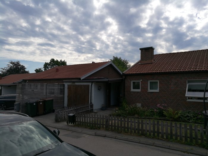 Exteriörvy av en tegelvilla med förrådsdel och lågt takprofil, en bil syns i förgrunden.