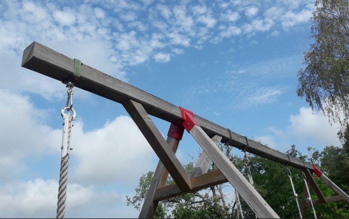 Träkonstruktion med extra snedstag och metallbeslag under en klar himmel.