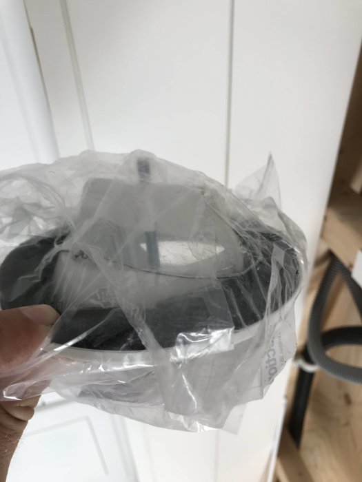 Hand håller rör med fästram i plastförpackning mot vit bakgrund.