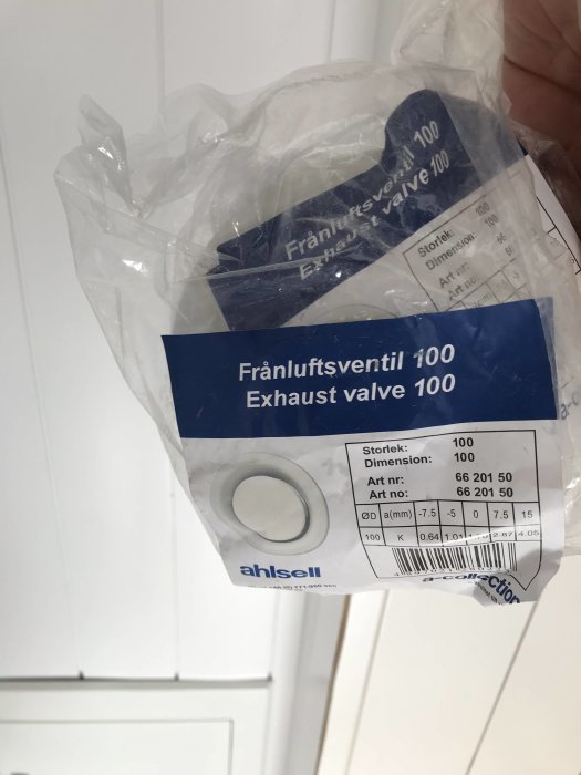 Plastförpackning hålls upp, visar frånlufstventil med etikett för storlek och artikelnummer på vit bakgrund.