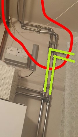 Rörinstallation med markerade T-rör och böjda rörledningar mot en vägg, synligt bakom ett draperi.