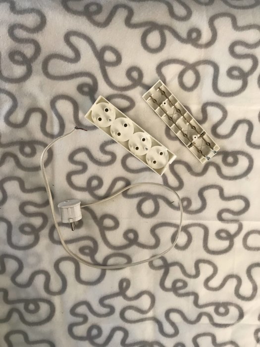 Elektrisk sladd med jordad hane och ett ojordat grenuttag på mönstrad bakgrund.