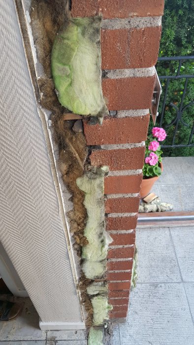 Isolerade träbitar mellan tegelfasad och inre vägg, synliga skruvändar och slitage, vid byggnadsrenovering.