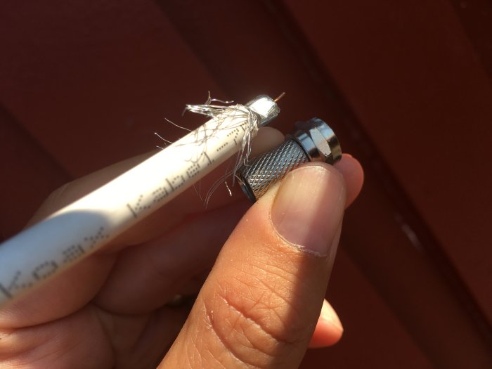 Hand som håller en avskalad koaxialkabel och en för liten metallkontakt.