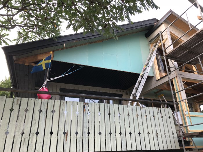 Hus under renovering med ny utegips och byggnadsställning, svensk flagga i förgrunden.