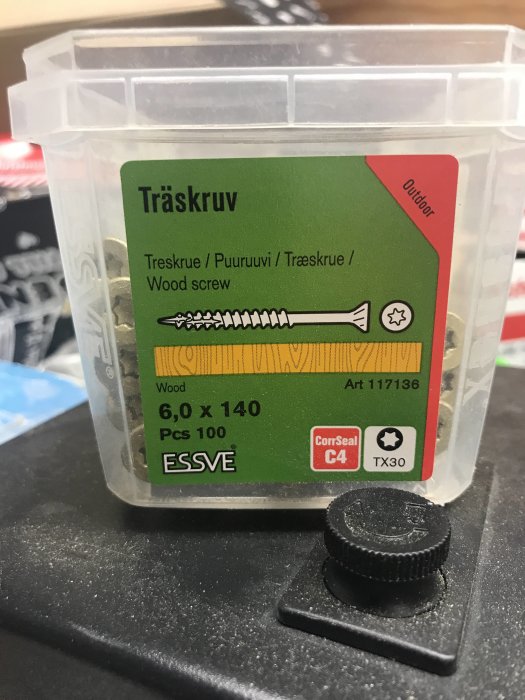 Trälåda med etikett för träskruvar 6,0 x 140 mm och en svart skruvmejselspets framför.