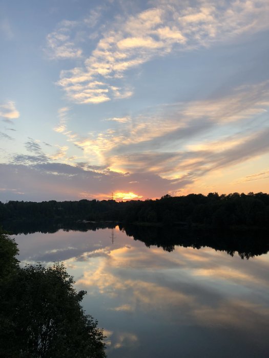 Solnedgång med färgstark himmel och moln reflekterade över en lugn vattenspegel.
