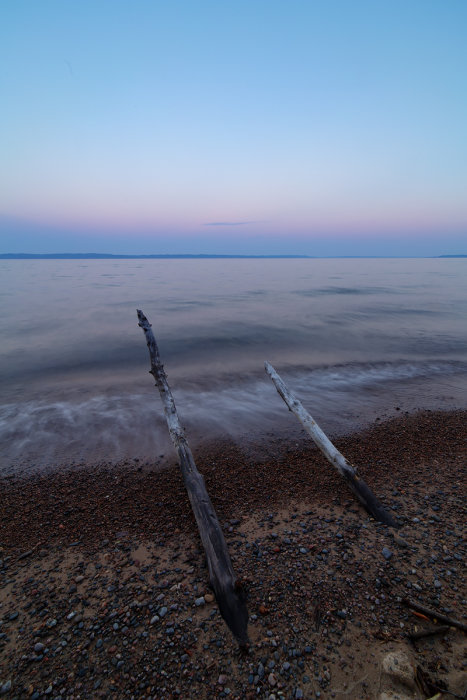 Kvällshimmel över Vättern med stenstrand och timmerstockar som leder ut i det stilla vattnet.