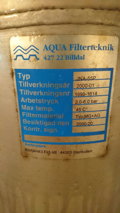 Specifikationsetikett på ett AQUA vattenfilter med filtermaterialbeteckning MG+AG och detaljerad produktinformation.