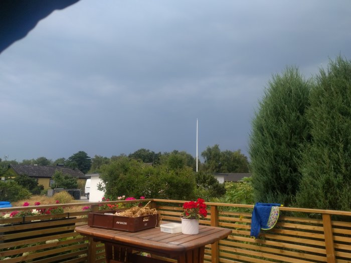 Mörka regnmoln i himlen ovanför en trädgård med en träaltan, blomlådor och en handduk som hänger på räcket.