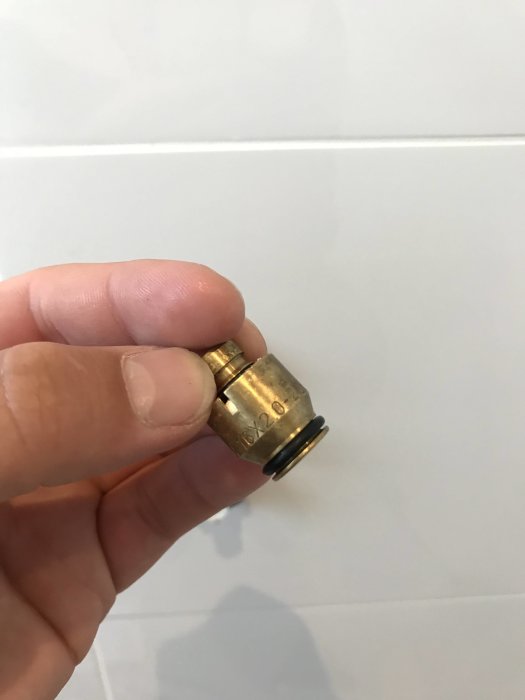 Hand håller en mässingsballofix med löstagbar huv och synlig O-ring framför vita kakelplattor.