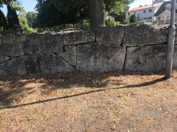 Rektangulär stenblocksmur i naturlig sten som omgärdar en trädgård.