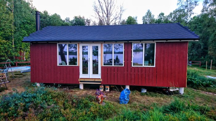 Rödmålad stuga med vita fönster och svart tak, nymålad med Demidekk färg, hängränna synlig.