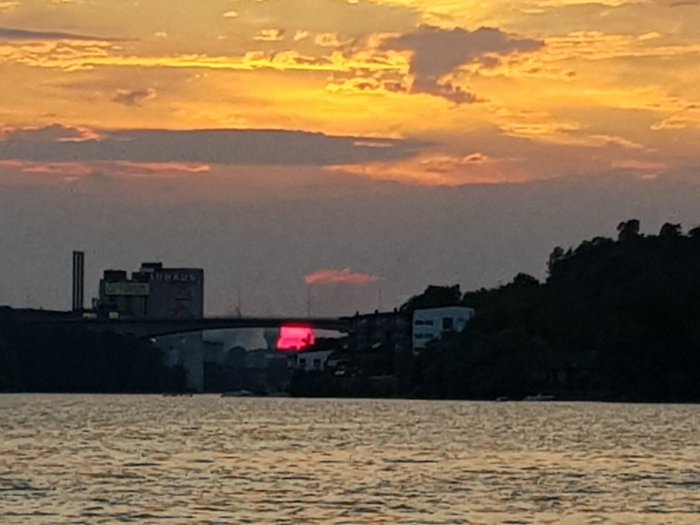 Solnedgång bakom en bro i Bälstaviken, Stockholm, med silhuetten av Pripps gamla bryggerier och radartorn vid Bromma flygplats.