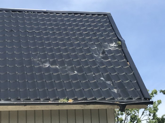 Svart tak med skador och smält plast under en klarblå himmel.