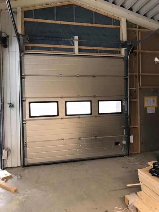 Industritakskjutport med fönster installerad i en byggnad, mindre bulor synliga nertill.