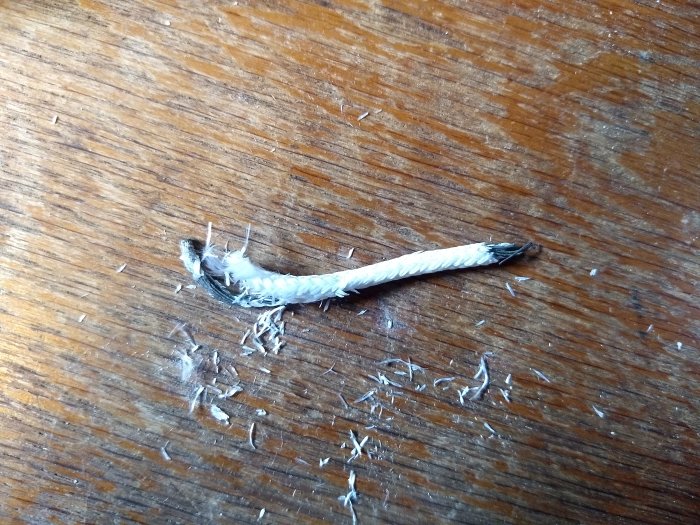 Skadad och isolerad elektrisk kabel med fransad isolering ligger på ett träbord, vilket indikerar slitage eller överhettning.