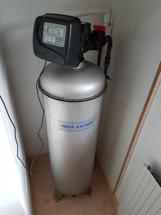 Vattenfilter från Aqua Expert med digital kontrollpanel installerat i ett hörn.