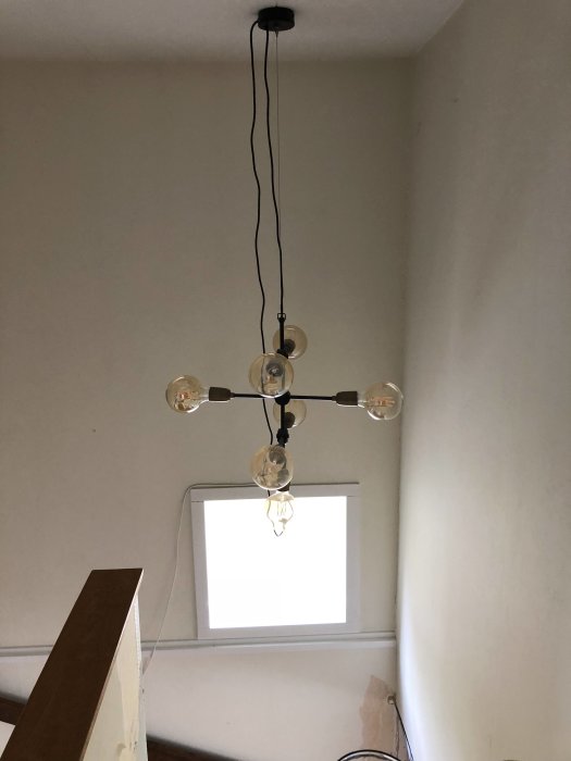 Nyinstallerat fönster i en trappa med en hängande lampa i förgrunden och en trästege.