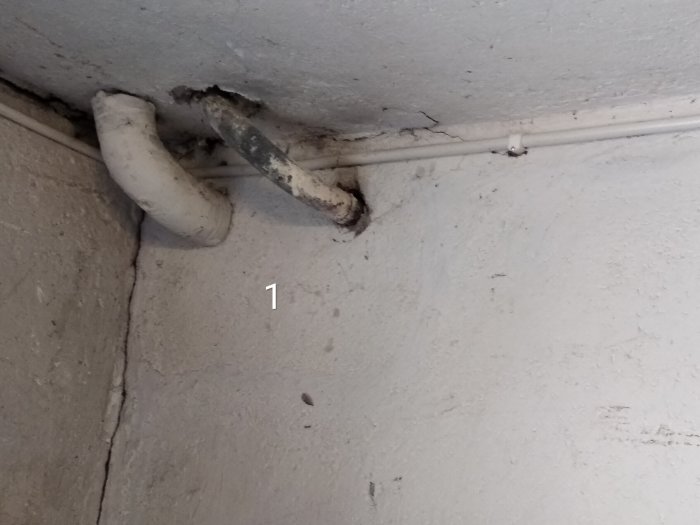 Gamla rörledningar som går längs och över ett vitmålat betongtak.