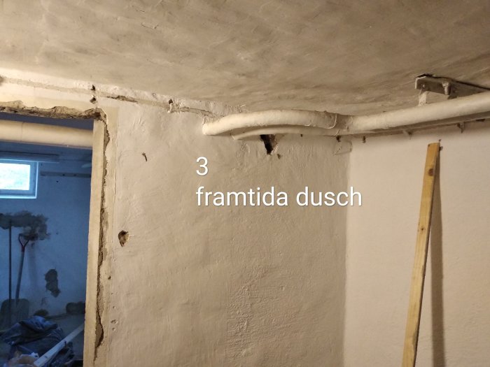 Renoveringsprojekt med synliga rör i taket och märkt utrymme för "framtida dusch".