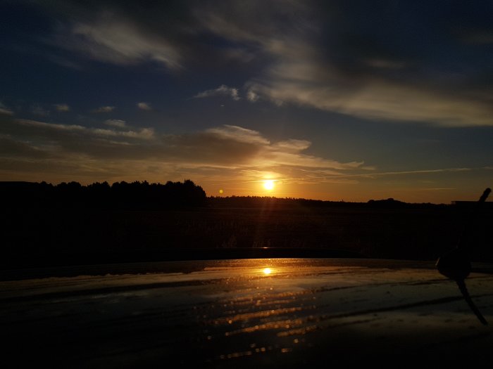 Soluppgång över ett fält sett från ett bilfönster med droppar på rutan.