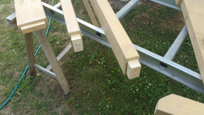 Grundmålade träbenställningar på gräs intill en metallstege, förberedda för limning.