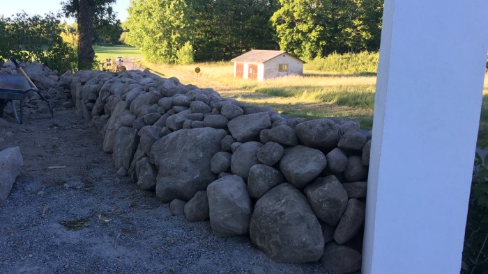 Stenmur byggd av runda stenar i två rader med en grusgång i mitten, omgiven av grönska.